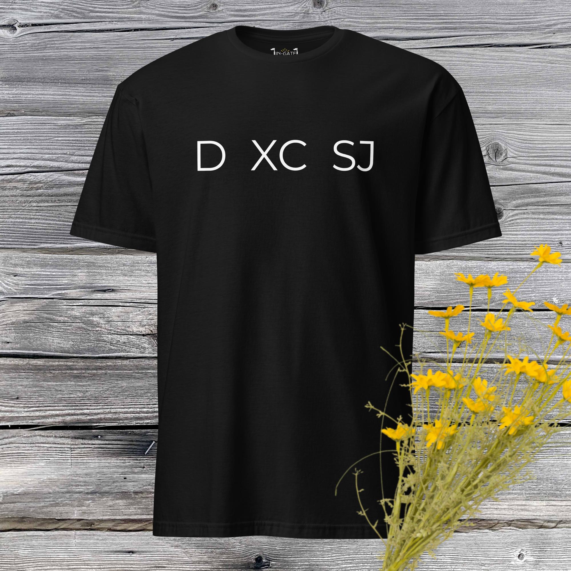 a black, short sleeve t-shirt with D xc and SJ across the chest in white against a weathered barn board wall and yellow flowers in the corner
